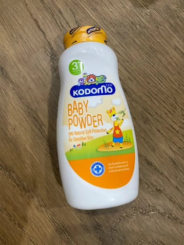 High-angle view of Kodomo Baby Powder 3+ orange bottle resting on a wooden surface.