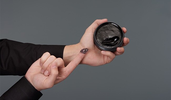 Hand holding the round container of Gatsby Edgy Quiff Pomade, showing the product size and texture.