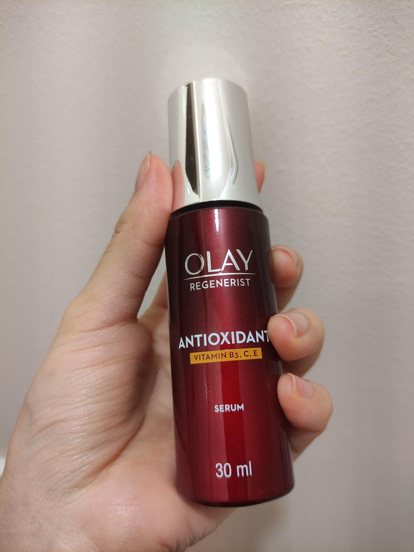 Hand holding Olay Regenerist Antioxidant Serum showing red bottle and silver pump