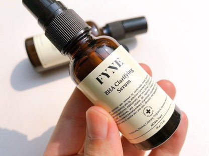 Hand holding an open bottle of FYNE BHA Clarifying Serum with dropper visible