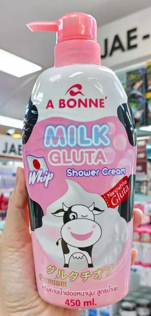 Hand holding an A Bonne Milk Gluta Shower Cream bottle in a store setting showing front label details.