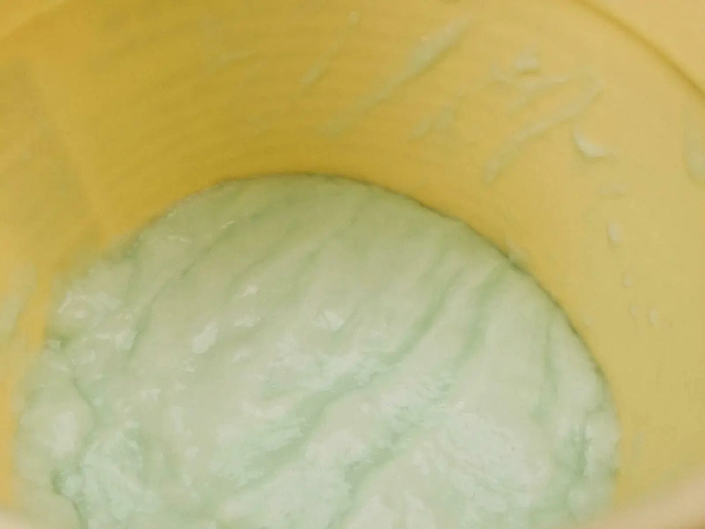 Caring AHA Hair Treatment formula in a yellow container, showcasing its creamy, green texture for nourishing damaged hair.