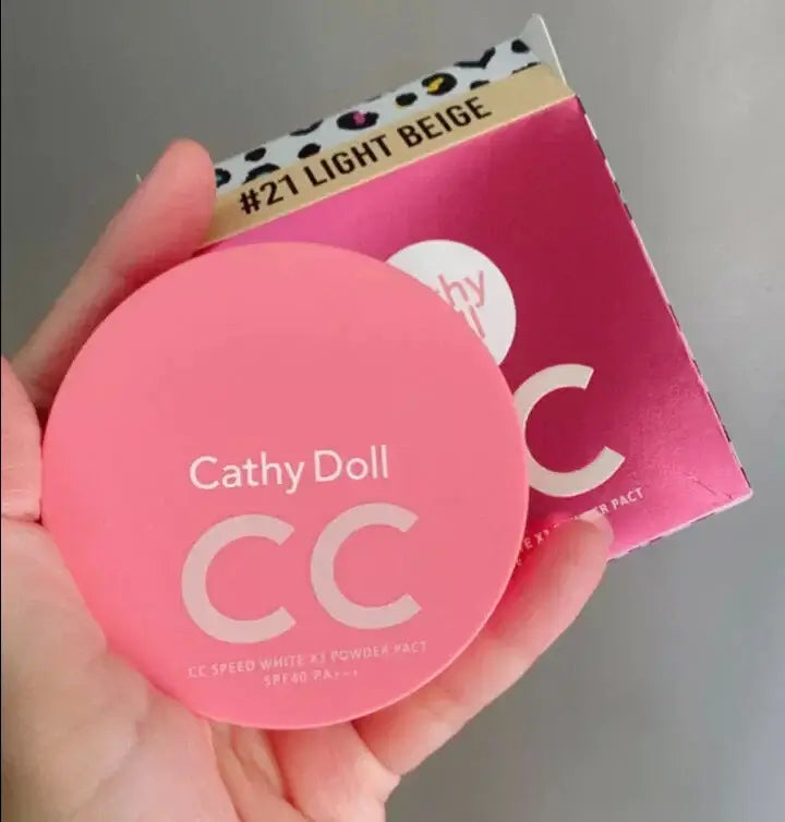 Hand holding pink Cathy Doll CC Powder Pact compact next to retail packaging box.