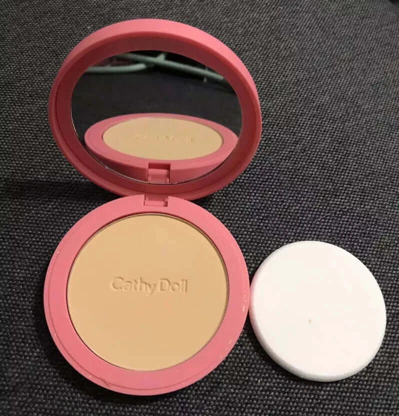 Cathy Doll CC Powder Pact open compact with built-in mirror, powder pan, and makeup puff on dark background.