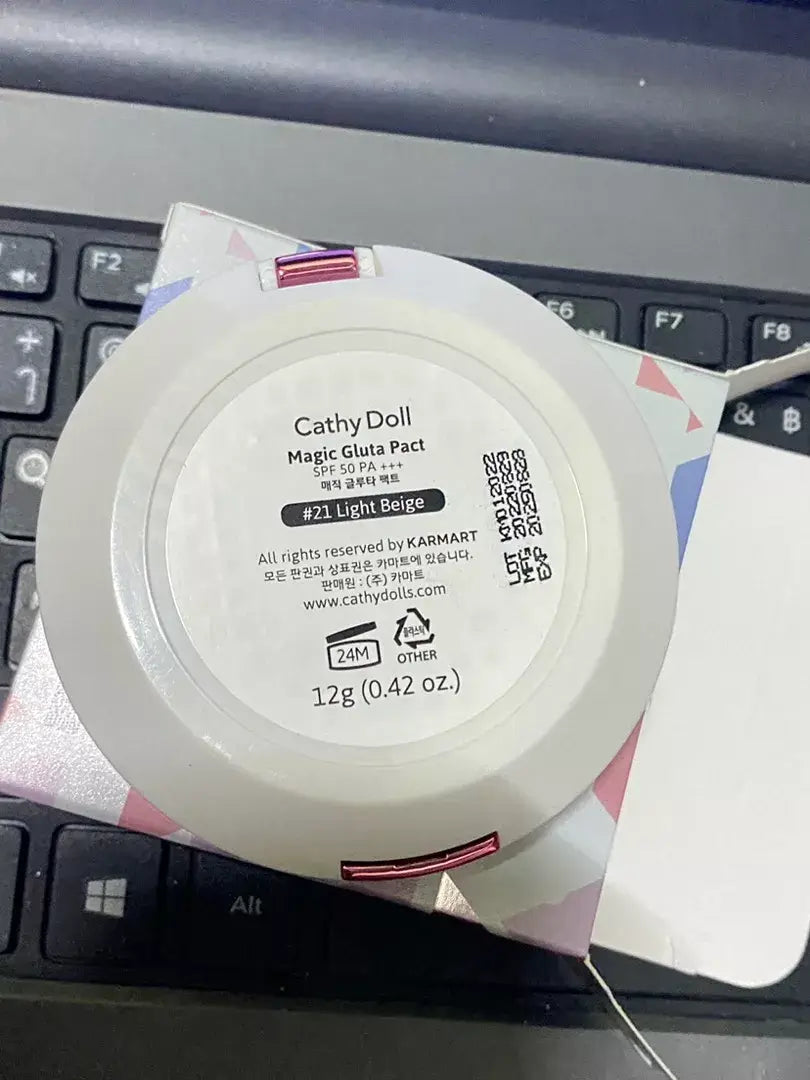 Cathy Doll Magic Gluta Pact SPF50 PA+++ #21 Light Beige compact face powder packaging on a laptop.