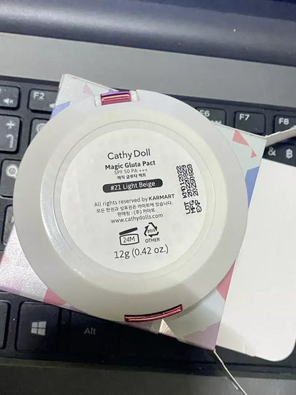 Cathy Doll Magic Gluta Pact SPF50 PA+++ #21 Light Beige compact face powder packaging on a laptop.