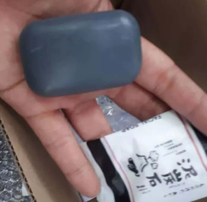 Deitanseki Charcoal Clay Soap held in a hand, featuring a gray color and packaged branding, 30g product from Japan.