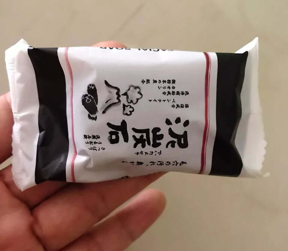 A person holding a single package of Deitanseki Charcoal Clay Soap in their hand to display its size.