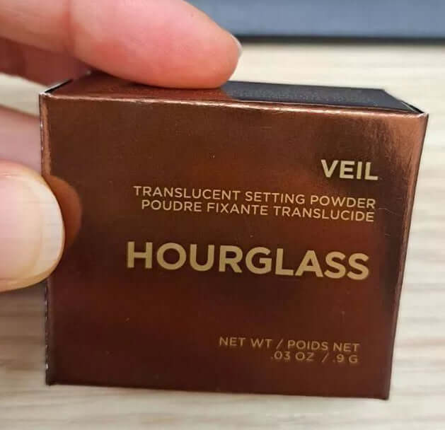 Hourglass Veil Setting Powder packaging, translucent loose face finishing powder, 0.9g, displayed in hand.