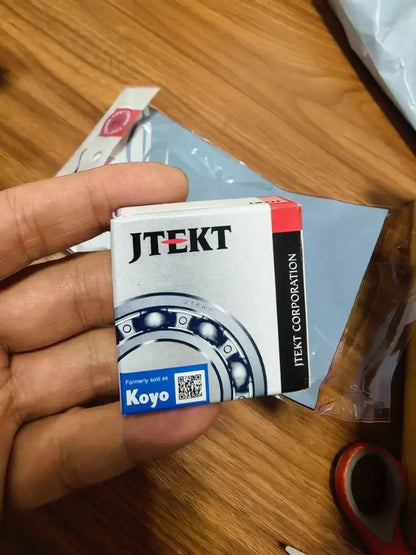 Hand holding KOYO packaging for KOYO 6203-2RS Bearing from JTEKT Corporation.