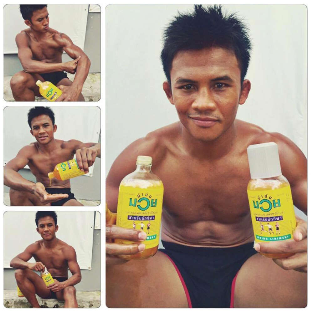 Namman Muay Liniment Oil athlete demonstration showing a boxer applying and holding the yellow Namman Muay Liniment Oil 120cc bottle for muscle warm-up and recovery training.