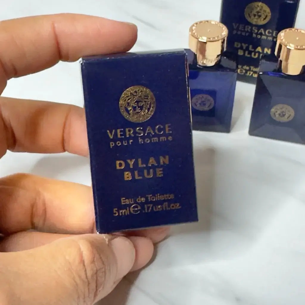 A close-up of a hand holding the bottom part of a Versace Dylan Blue Pour Homme EDT bottle.
