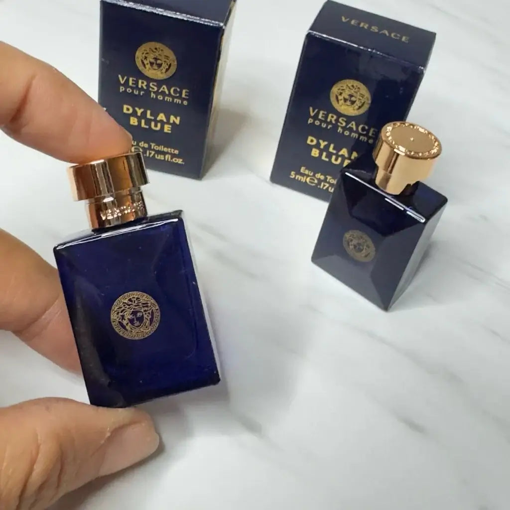 A hand holding a miniature bottle of Versace Dylan Blue Pour Homme EDT with its box.