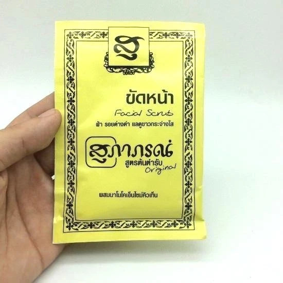 A close-up of a white sachet of Supaporn Facial Scrub being held in a hand.