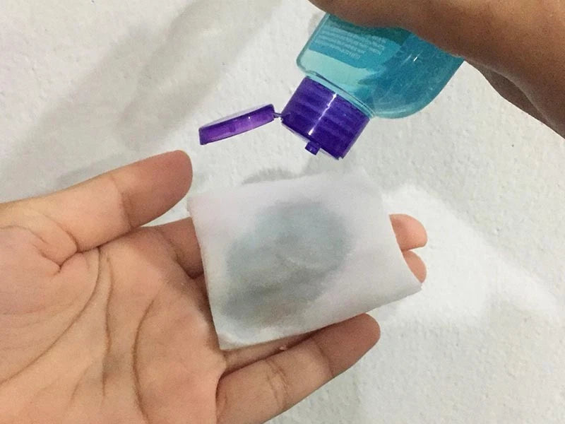  Hand holding Clean & Clear Oil-Control Toner bottle dispensing product onto cotton pad.