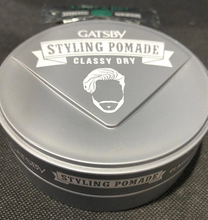Angled view of the GATSBY Classy Dry Pomade jar and lid with white ribbon text.