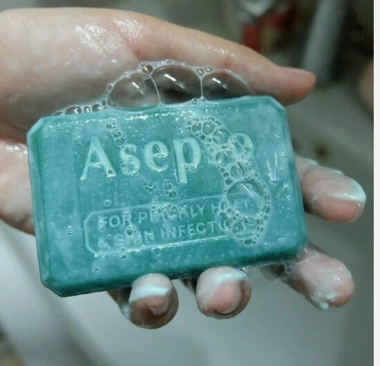 A hand holding a lathered-up Asepo green soap bar, highlighting the suds and the product's use.