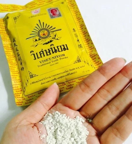 Viset Niyom Tooth Powder being poured onto a hand to show the fine white herbal powder texture