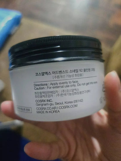 Hand holding COSRX Advanced Snail Mucin 92 All in One Cream jar front label