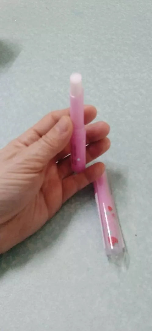 Hand holding MISTINE Pink Magic Lip Balm Strawberry Vitamin E 1.7g with another tube lying on a flat surface