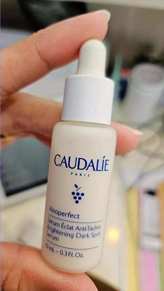 Person holding Caudalie Vinoperfect Serum 10ml bottle close up indoors