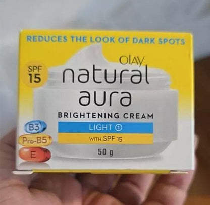 Hand holding Olay Natural Aura Cream cardboard box showing product benefits