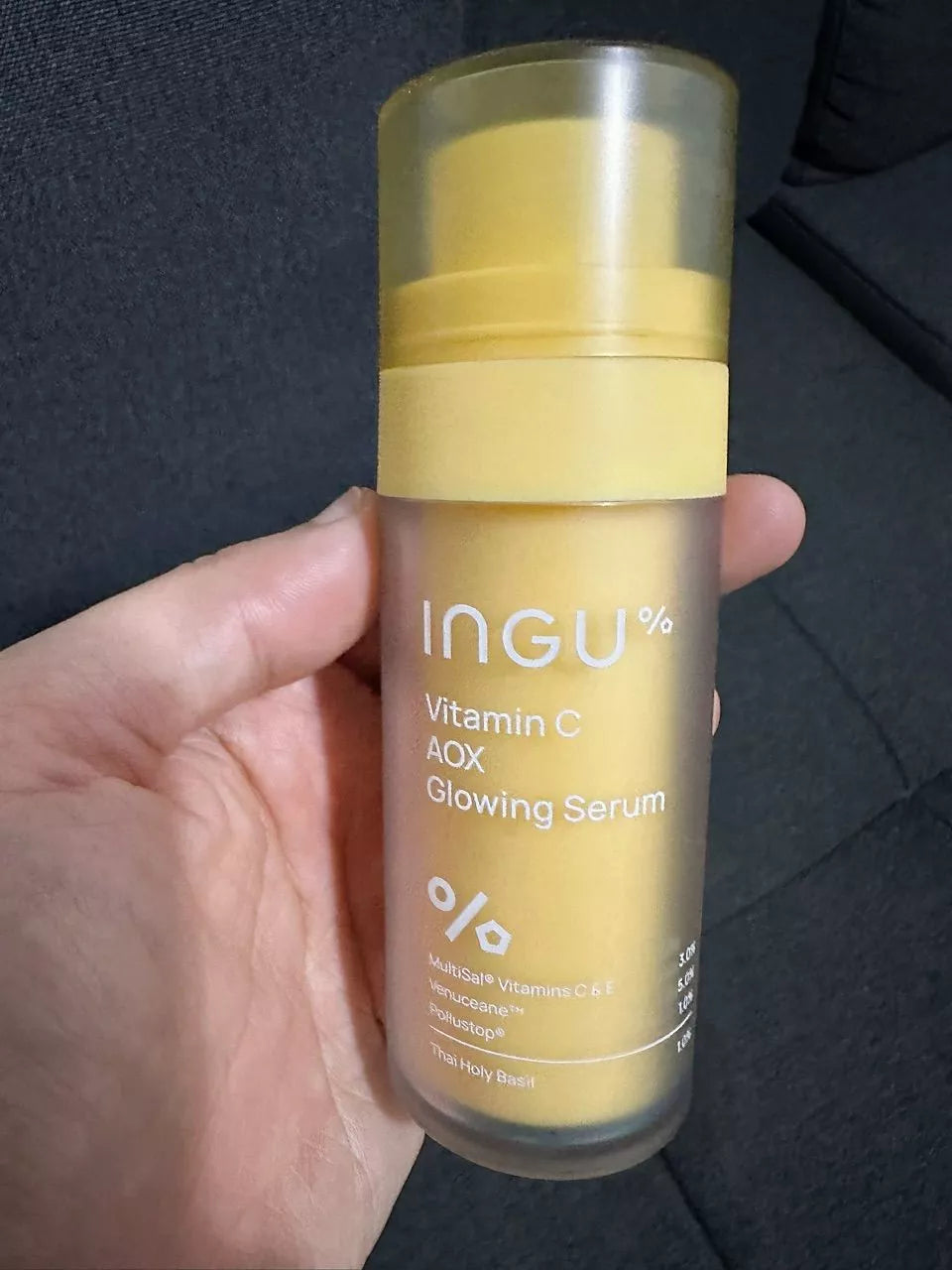 Hand holding INGU Vitamin C AOX brightening serum bottle in natural lighting